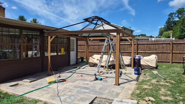 Hardtop pergola kit being assembled on a paver patio in Moon Township, PA, with the frame and roof structure in progress.